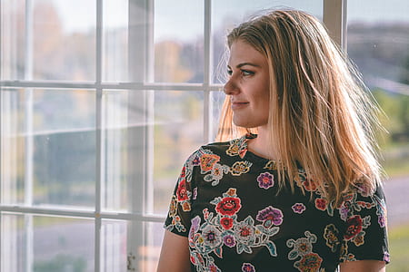 woman wearing multicolored floral crew neck t-shirt near window during daytime thumbnail