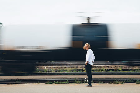 A long haired young caucasian man standing near passing train thumbnail