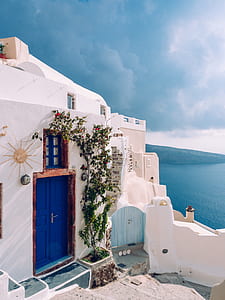 white concrete house near body of water under blue and white sky during daytime photography thumbnail