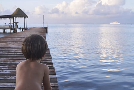 boy sitting on dock facing body of water thumbnail