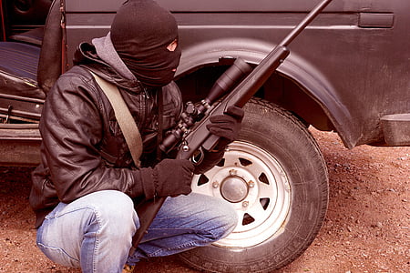 man sitting beside car while holding a rifle thumbnail