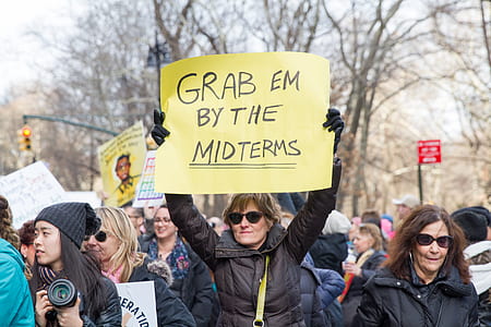 woman raising poster with grab em by the midterms text thumbnail