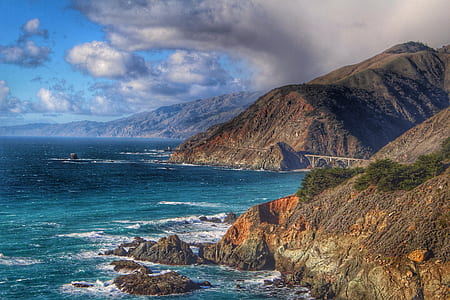 cliff near body of water under cloudy sky thumbnail