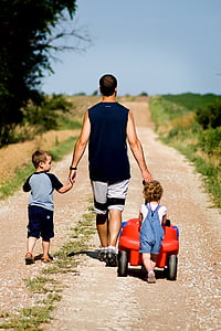 man walking with two children on brown road thumbnail