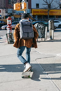 Man Wearing Brown Jacket, Blue Denim Jeans, and White Shoes Riding Skateboard on Sideway thumbnail