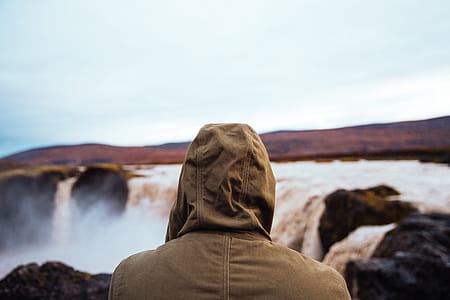Hiker in a hooded jacket watching the waterfall on a cloudy day thumbnail