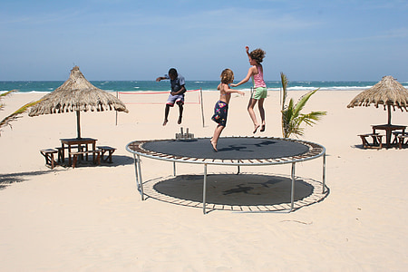 three children playing on round black trampoline near beach at daytime thumbnail