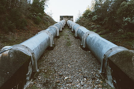 two large grey metal pipes between trees thumbnail