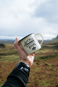 person holding beige quote-printed mug with mountains background thumbnail