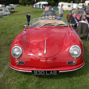 selective focus of red cabriolet on grass field thumbnail