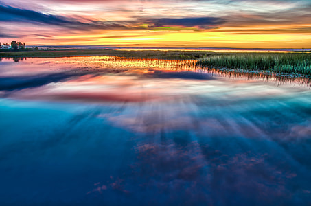 body of water beside of grass during sunrise thumbnail