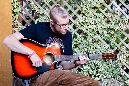 man playing acoustic guitar near brown wall thumbnail