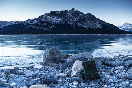 green backpack on grey rocks with distance to mountain thumbnail