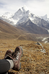 depth of field photography of person wearing brown leather hiking boots in front of mountains during daylight thumbnail
