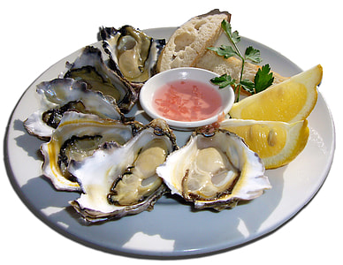 oyster shell with sauce and sliced lemon on white ceramic plate thumbnail
