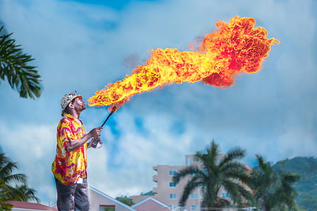 man in yellow and red top blowing fire under white clouds and blue sky during daytime thumbnail
