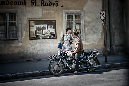 man riding motorcycle parked on road while taking to woman thumbnail