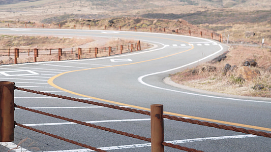 grey curving road with brown fence during daytime thumbnail