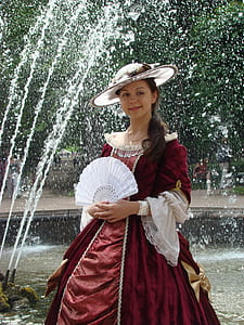 woman holding white hand fan standing near water fountain thumbnail