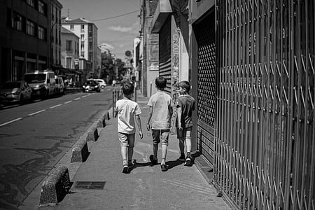 grayscale photo of three boys walking near road thumbnail
