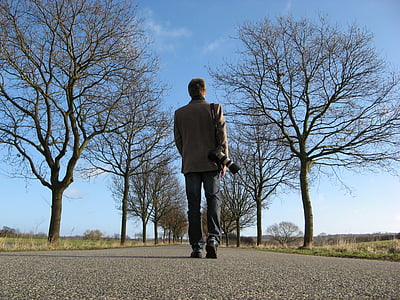 man in brown suit jacket and black jeans walks on gray asphalt road thumbnail