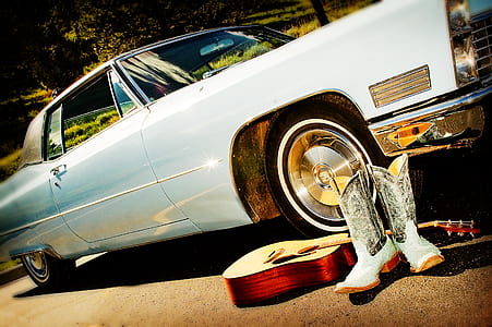 pair of white-and-gray cowboy boots and guitar beside vintage white coupe thumbnail