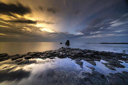 long exposure time lapse photo of rocky shore with ocean on the horizon during twilight thumbnail