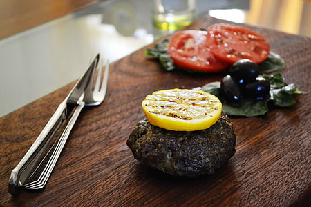 well done meat with lime on top near sliced tomatoes and flatware on brown board thumbnail