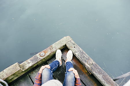 person sitting on dock facing body of water during daytime thumbnail