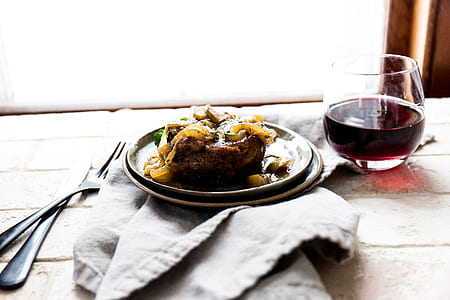 cooked meat on plate beside glass of wine thumbnail