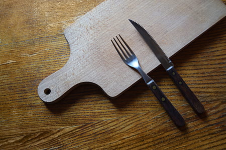 stainless steel fork beside knife on top of wooden chopping board thumbnail