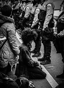 grayscale photo of man kneeling in front of cops forming line thumbnail