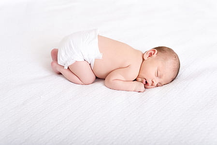 baby in white disposable diaper sleeping on white cushion thumbnail