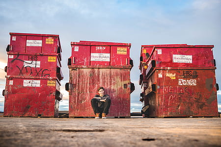 man sitting in front of red containers thumbnail