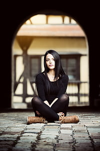 woman wearing black crew-neck top ad leggings and brown leather boots sitting on grey brick floor thumbnail