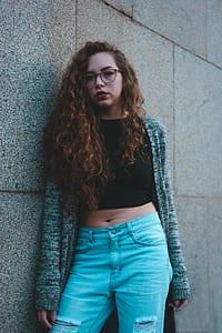woman wearing black crop top and blue jeans leaning on gray concrete wall thumbnail