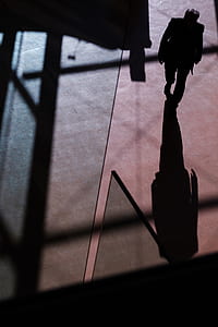 silhouette of man walking towards his shadow on orange concrete floor thumbnail