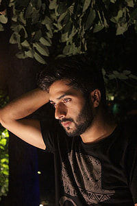 man in black t-shirt holding hes head under green leaf tree during night time thumbnail