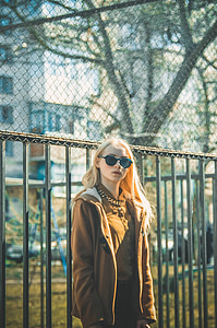 woman wearing brown zip-up jacket and sunglasses near metal framed fence during daytime thumbnail