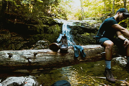 man sitting on brown tree trunk above creek thumbnail
