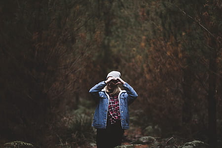 woman standing surrounded by trees while making hand heart sign thumbnail