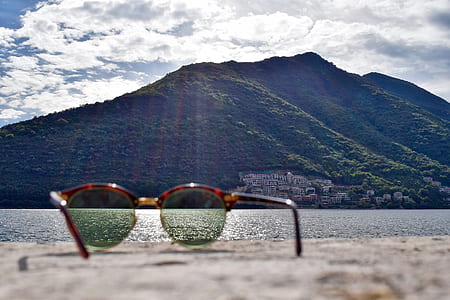 brown framed sunglasses facing mountain and body of water during day thumbnail