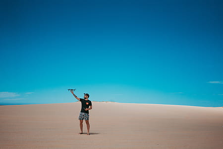 man wearing black t-shirt and gray shorts standing on dessert field landscape photography thumbnail