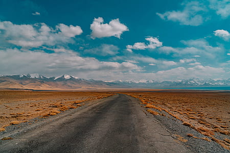 landscape photography of black road near brown grass field under cloudy blue sky thumbnail
