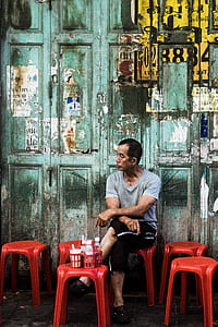 man sitting on red plastic stool outdoor at daytime thumbnail