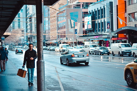man in black coat walking on the street near cars thumbnail