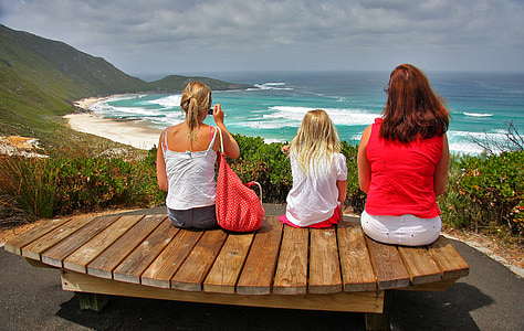 women sitting on brown wooden bench looking at ocean thumbnail