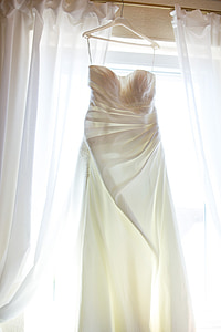 white drape tube wedding gown hang on clothes hanger against window curtains thumbnail