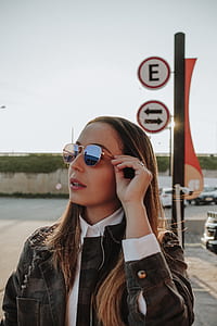 woman wearing green, beige, and black camouflage jacket with eyeglasses near signage thumbnail