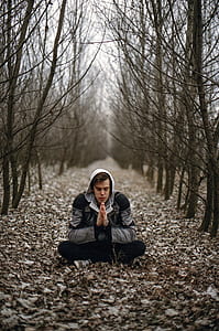 man wearing gray jacket and black pants meditating on road with dried leaves near trees thumbnail